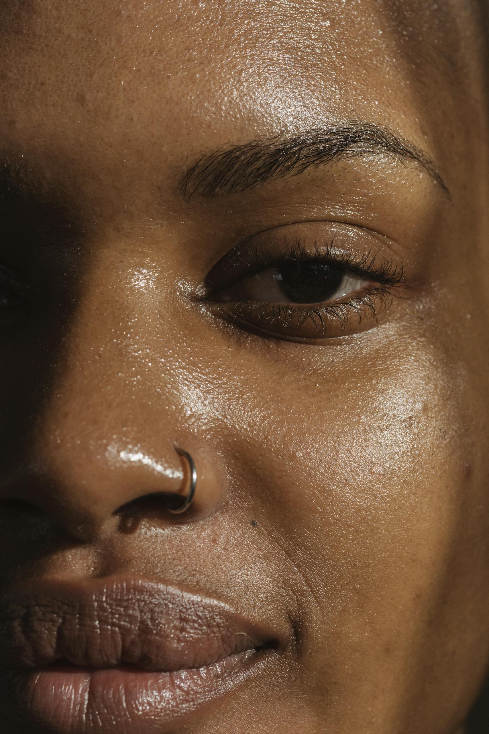 A detailed close-up of a woman's face highlighting her skin texture and nose ring.